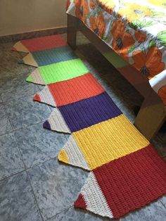 multicolored crocheted rugs on the floor next to a bed