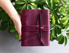 a person holding a purple book with a black pen in it and green leaves behind them