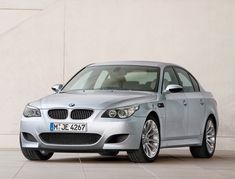 a silver car is parked in front of a white wall and some concrete flooring