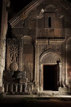 an old church with carvings on the front and side walls, lit up at night