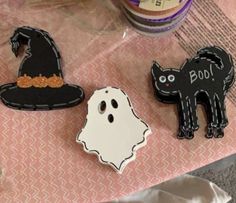 three decorated halloween cookies sitting on top of a pink table cloth covered with white and black icing