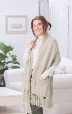 a woman standing in front of a white couch wearing a shawl and green pants