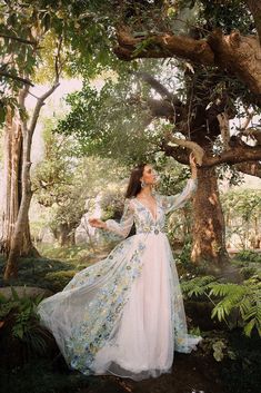 a woman in a long dress standing under a tree with her arms outstretched and hands out