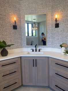 a woman taking a selfie in the mirror of a large bathroom vanity with wooden cabinets and drawers