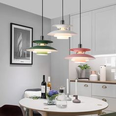 a dining room table with four lights hanging from it's ceiling and two vases on the table