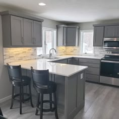 a kitchen with gray cabinets and white counter tops, black bar stools in front of an island