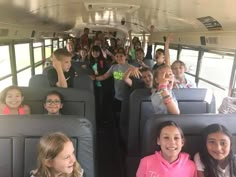 a group of children sitting in the back of a bus with their hands up and smiling