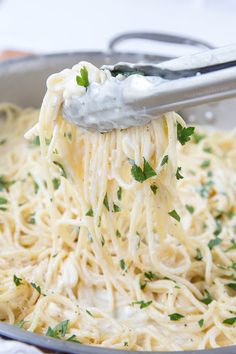 a fork full of spaghetti being lifted from a pan with sauce and parsley on top