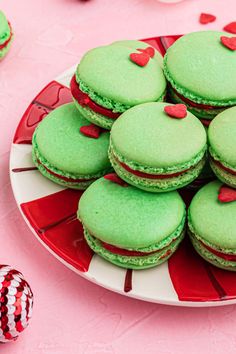 a plate full of green macaroons with red hearts on them sitting on a pink tablecloth