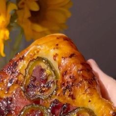 a close up of a person holding a piece of food in front of yellow flowers