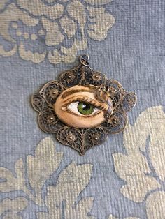 "Hand-painted Lover's Eye vintage silver filigree pendant. This piece of jewelry is a one of a kind, hand-painted by me on a vintage piece of jewelry selected also by me. It's painted with acrylic paint and varnished for protection and signed on the inside of the pin. The pendant is 1 3/4 wide x 1 1/2 inch wide. It comes with a silver plated chain - 18 inches long. \"The lover's eye is an 18th century variation on a portrait miniature of a secret love which typically displayed only the eye and e Bohemian Pendant Jewelry For Art Collection, Vintage Hand-painted Pendant Necklace, Vintage Hand Painted Pendant Necklace, Vintage Hand Painted Round Pendant Necklace, Bohemian Hand Painted Jewelry For Art Collection, Vintage Hand Painted Pendant Jewelry, Handmade Wearable Art Jewelry For Art Collection, Vintage Hand Painted Jewelry Gift, Vintage Hand Painted Jewelry For Gift