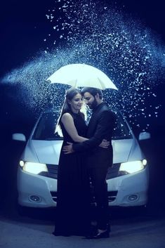 a man and woman standing under an umbrella in front of a car with water splashing all over them