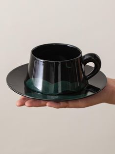 a hand holding a black coffee cup and saucer