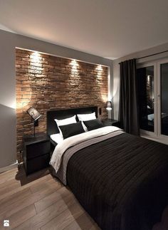 a bedroom with a brick wall behind the bed and wooden flooring is lit by recessed lights