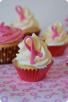 several cupcakes with pink and white frosting on a tablecloth, one has a pink ribbon