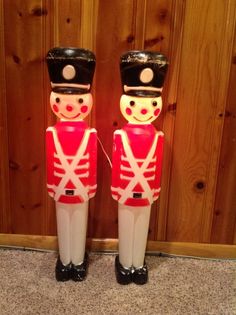 two toy soldiers standing next to each other in front of a wood paneled wall