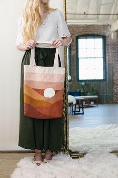 a woman standing in front of a mirror holding a large bag with an orange and pink design on it