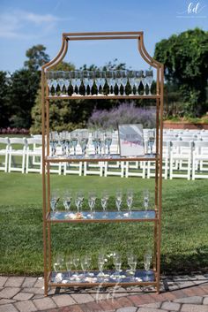 many champagne flutes are displayed on a gold metal framed shelf with glass panels. there are four tiers of champagne glasses for wedding guests to consume. champagne wall/champagne display adjustable per headcount Champagne Shelf, Gold Shelf, Gold Shelves, Cocktail Hour Wedding, Wedding Display, Champagne Toast