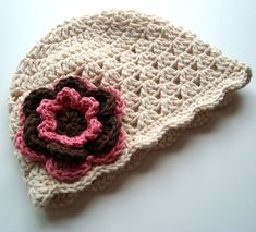 a crocheted hat with a pink flower on the front and brown trim around it