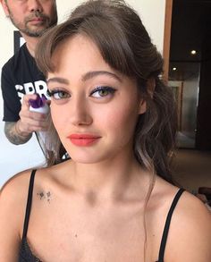 a woman is getting her hair done by a man in the background with an object on his head