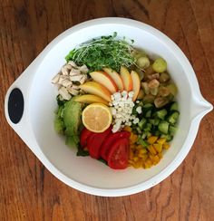 a white bowl filled with lots of different types of fruits and vegetables on top of a wooden table