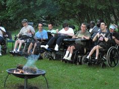 several people sitting in wheelchairs around a fire pit while others watch from the grass