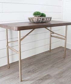 a table with a bowl on it and a plant in the middle, against a white wall