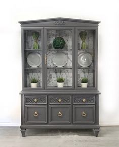 a gray china cabinet with plants and plates on it