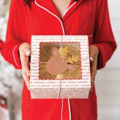 a woman in red pajamas holding up a box with a reindeer cut out on it