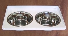 two stainless steel dog bowls on a white plastic tray with wooden background and wood grain flooring