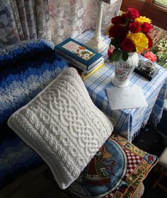 a blue and white table topped with pillows and a vase filled with flowers next to a window