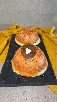 two bagels with salmon on them are sitting on a black plate next to a yellow towel