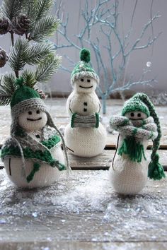 three knitted snowmen with hats and scarfs around them, standing next to a pine tree