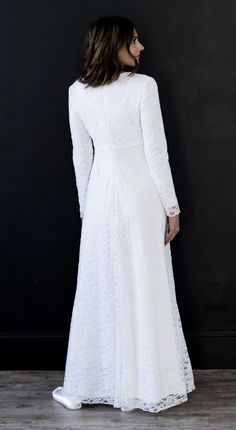 a woman wearing a white dress standing in front of a black wall with her back turned to the camera