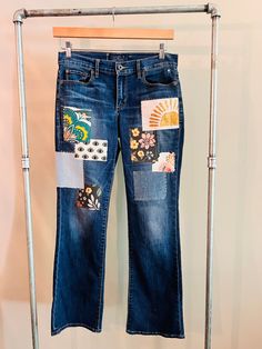 a pair of blue jeans with patches and flowers on them hanging from a clothes rack