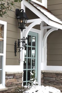 the front door of a house with a light on it's side and snow on the ground