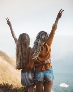 two young women standing on top of a hill with their arms up in the air