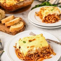 two white plates topped with lasagna covered in cheese and sauce next to bread