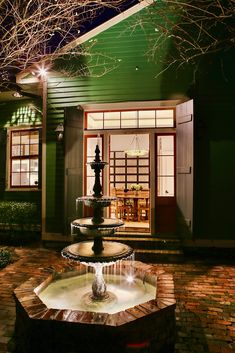 a fountain in front of a green house at night with lights on the windows and doors