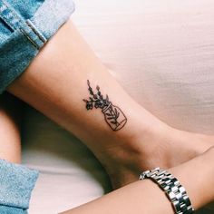 a woman's foot with a small tattoo on her left ankle and flowers in the vase