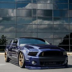 a blue mustang with gold rims parked in front of a building