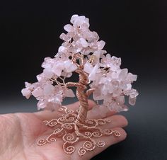 a hand holding a wire wrapped tree with pink crystals on it's branches and roots