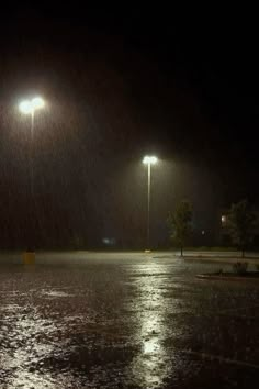 an empty parking lot at night in the rain with street lights and no one on it