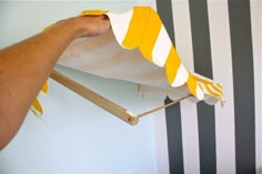 a hand holding a yellow and white striped umbrella over a wall with black and white stripes on it