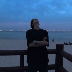 a man is looking up at the sky while standing on a boardwalk near the beach