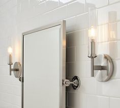 a bathroom mirror with two lights and a light on the wall next to it in front of a white tiled wall