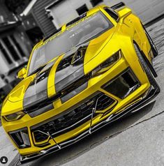 a yellow sports car parked in front of a garage with the hood up and stripes on it