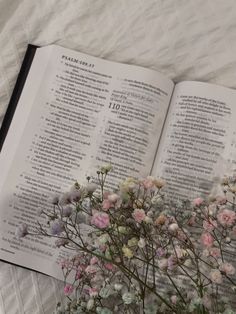 an open book on a bed with flowers in the foreground and text above it