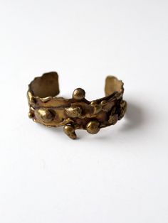 "This is a 1960s vintage brutalist brass cuff. The hand-crafted piece features intricate cast detailing with a striking patina.  CONDITION In good condition with wear consistent with age and use. MEASUREMENTS Length:  5.5\"  ...  14 cm Width:  1.25\"  ...  3.2 cm SHOP MORE CUFFS from 86 Vintage https://www.etsy.com/shop/86Vintage86/search?search_query=cuff+jewelry 111598" Vintage Brass Cuff Jewelry, Bronze Brass Cuff Bracelet, Antique Gold Brass Cuff Bangle Bracelet, Vintage Bronze Cuff Jewelry, Vintage Gold Hand Cast Cuff Bracelet, Vintage Cuff Bracelet With Patina, Bronze Antique Finish Cuff Bracelet Bangle, Hand Cast Bronze Metal Cuff Bracelet, Bronze Metal Bracelet With Patina