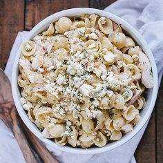 a white bowl filled with pasta and cheese on top of a wooden table next to a spoon